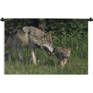 Wandkleed Wolven - Wolf met jong in het gras Wandkleed katoen 90x60 cm - Wandtapijt met foto