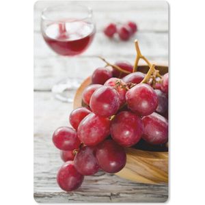 Tros rode druiven in kommetje naast een glas rode wijn