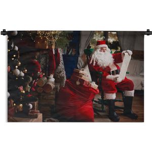 Wandkleed Kerst - De kerstman zittend in een stoel met zak vol geschenken Wandkleed katoen 150x100 cm - Wandtapijt met foto