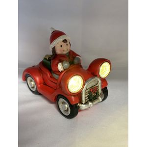 Kerstbeeldje meisje in rode auto met LED - koplampen + groen cadeau - polyresin - 12 cm hoog x 16 cm x 8 cm – Kerstdecoratie