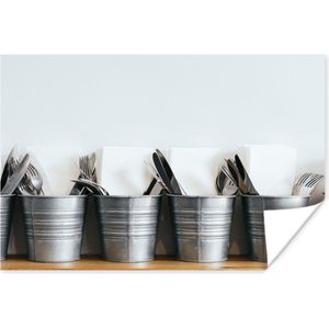 Metalen emmers met verschillende soorten bestek en servetten die op een houten plank tegen een witte muur staan 120x80 cm