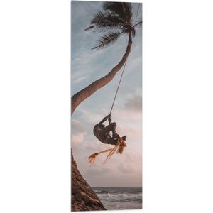 WallClassics - Vlag - Man Slingerend aan Kromme Palmboom - 30x90 cm Foto op Polyester Vlag