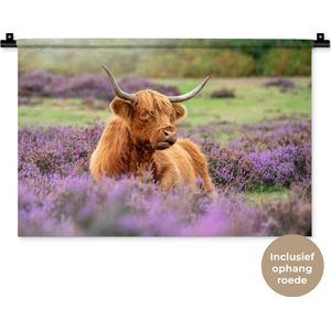 Wandkleed Schotse hooglander - Een Schotse hooglander ligt tussen de paarse bloemen Wandkleed katoen 60x40 cm - Wandtapijt met foto