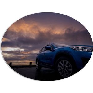PVC Schuimplaat Ovaal - Blauwe Auto in Regenbui onder Donkere Bewolking - 96x72 cm Foto op Ovaal (Met Ophangsysteem)