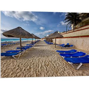 WallClassics - PVC Schuimplaat- Blauwe Ligbedden op Strand met Rieten Parasols - 100x75 cm Foto op PVC Schuimplaat