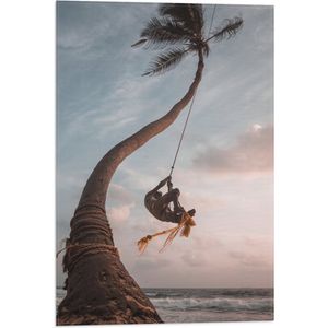 WallClassics - Vlag - Man Slingerend aan Kromme Palmboom - 40x60 cm Foto op Polyester Vlag