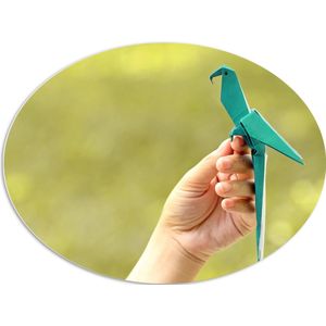 PVC Schuimplaat Ovaal - Blauwe Origami Vogel op Hand van Mens in Groene Omgeving - 96x72 cm Foto op Ovaal (Met Ophangsysteem)