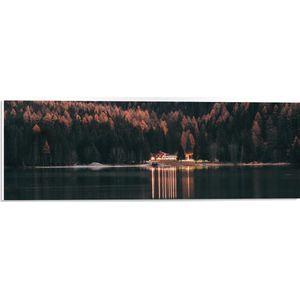 PVC Schuimplaat- Verlicht Gebouw aan Bosrand bij Open Meer - 60x20 cm Foto op PVC Schuimplaat