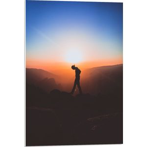 WallClassics - PVC Schuimplaat- Silhouet Persoon tussen de Bergen bij Zonsondergang - 50x75 cm Foto op PVC Schuimplaat