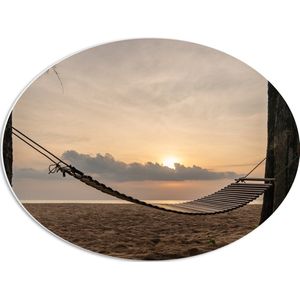 PVC Schuimplaat Ovaal - Houten Hangmat tussen Hoge Bomen op het Strand bij Ondergaande Zon - 56x42 cm Foto op Ovaal (Met Ophangsysteem)