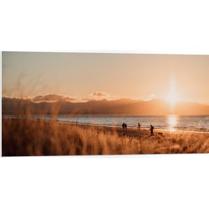 WallClassics - PVC Schuimplaat - Zon Verdwijnend achter Bergen bij Strand - 100x50 cm Foto op PVC Schuimplaat (Met Ophangsysteem)